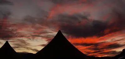 a silhouette of a pyramid with a sunset in the background at Memories Aicha Luxury Camp in Wadi Rum