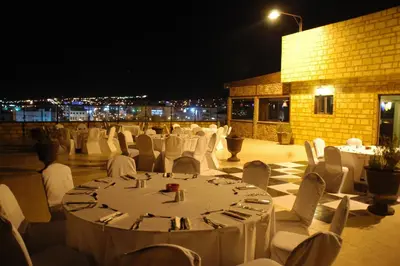 a banquet hall with white tables and chairs at night at Mina Hotel in Aqaba