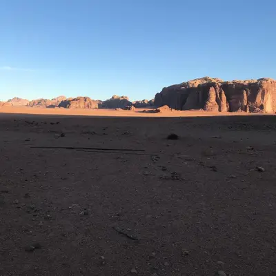 an empty desert with cliffs and rocks in the background at Bedouin House Camp in Wadi Rum