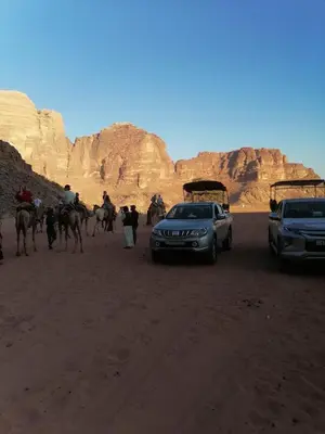 a group of people and camels and a car in the desert at Black Irish Camp And Tours in Wadi Rum