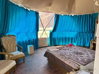 a bedroom with blue curtains and a bed and a chair at Jamal Rum desert in Wadi Rum