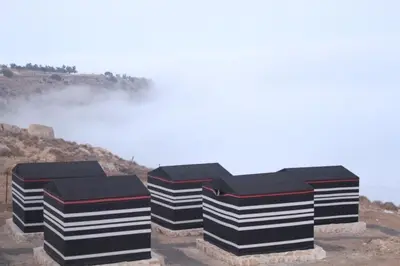 three black and white boxes on a hill with fog at Ein lahda camp-site in Dana