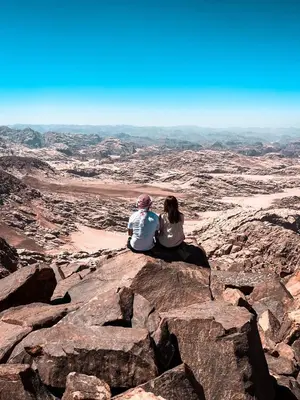 two people sitting on a rock in the desert at Bedouin Holidays Camp and Jeep Tours in Wadi Rum