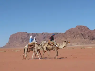 three people riding on the backs of camels in the desert at Salem Camp in Wadi Rum