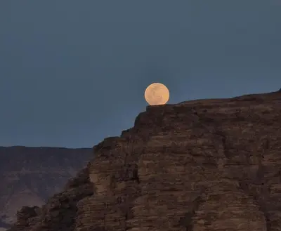 a full moon sitting on top of a cliff at Wadi Rum Bubble Camp in Wadi Rum
