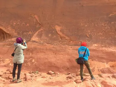 two women taking pictures of a rock wall at WADI RUM-Bedouin Tents and Jeep Tours in Wadi Rum