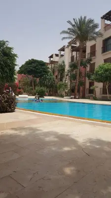 a swimming pool in front of a building with palm trees at Sea View Apartment at Tala Bay Resort in Aqaba in Aqaba
