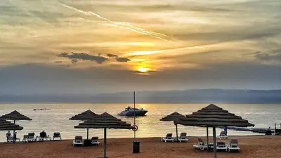 a beach with umbrellas and a boat in the water at Sea View Apartment at Tala Bay Resort in Aqaba in Aqaba