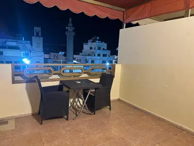 a small table and chairs on a balcony at night at Relax House For Studio Rooms Apartments ريلاكس هاوس للشقق المفروشة in Aqaba