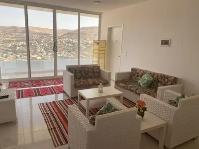 a living room with chairs and a table and windows at Jordan Guest House in Wadi Musa