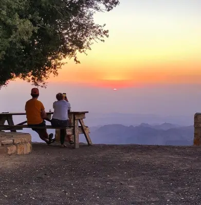 two people sitting on a picnic table watching the sunset at Jabal Dana Hotel - the highest hotel in Jordan in Dana