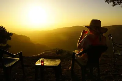 a woman sitting in a chair watching the sunset at Jabal Dana Hotel - the highest hotel in Jordan in Dana