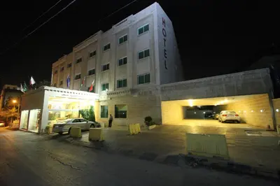 a building with cars parked in a parking lot at night at Al Thuraya Hotel in Amman