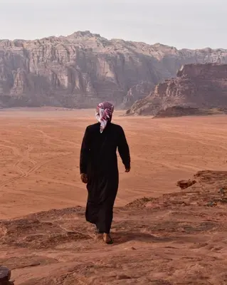 a man in black walking through the desert at RUM SOlARIS BEDOUIN CAMP in Wadi Rum
