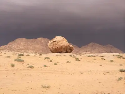 a rock in the desert with mountains in the background at Magic Wadi Rum in Wadi Rum