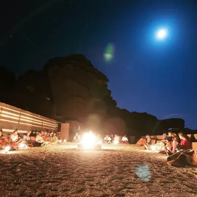 a group of people sitting around a fire at night at Wadi Rum Excursions in Wadi Rum