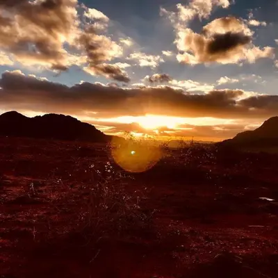 a sunset in a field with the sun setting at Wadi Rum Excursions in Wadi Rum