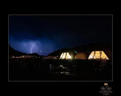 a lightning storm over a field with two domes at Wadi Rum UFO Luxotel in Wadi Rum