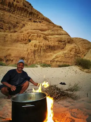 a man sitting next to a pot of fire at Wadi Rum Old Bedouin Camp in Wadi Rum
