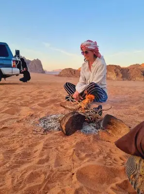 a man sitting in the desert with a campfire at Qais Camp Wadi Rum in Wadi Rum