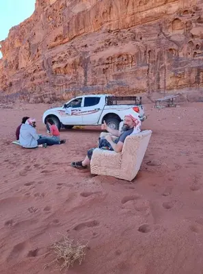 a group of people sitting in the sand next to a truck at Qais Camp Wadi Rum in Wadi Rum