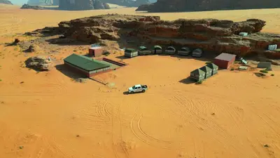 a white truck parked in a desert with buildings at Wadi rum Local guide camp in Wadi Rum