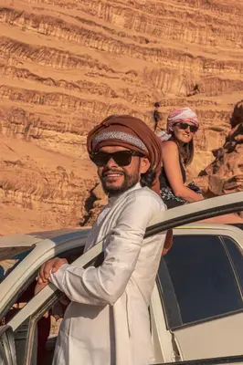 a man standing next to a car with a woman at Wadi Rum Pyramids Camp in Wadi Rum