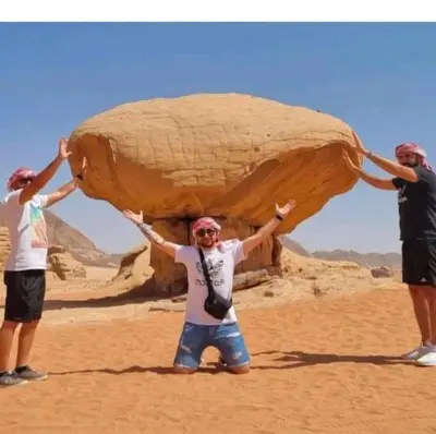 three people holding up a large rock in the desert at Landscape Rum Camp in Wadi Rum