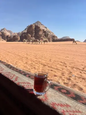 a glass of drink sitting on a table in the desert at Landscape Rum Camp in Wadi Rum
