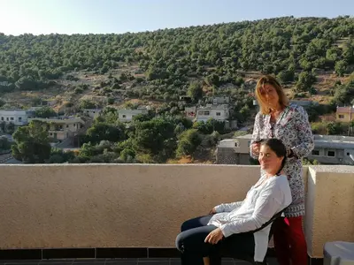two women sitting on the edge of a ledge with a view at Mhna guest house بيت الضيافة الريفي in Ajloun