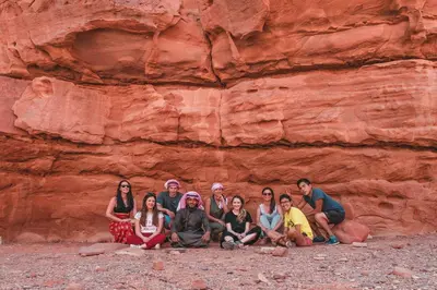 a group of people sitting in front of a cliff at wadi rum bedouin stars camp in Wadi Rum