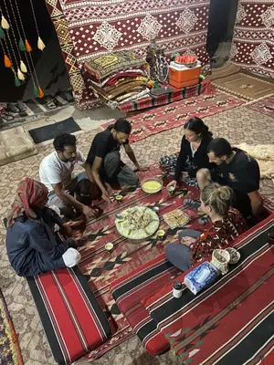 a group of people sitting around a table with pizza at Wadi Rum Desert Base Camp in Wadi Rum