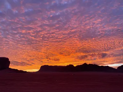 a sunset on the beach with rocks in the background at Khazali Mountain Camp in Wadi Rum