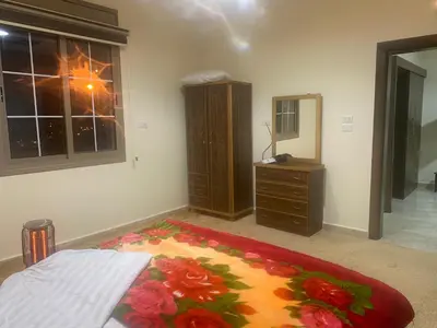 a bedroom with a bed and a dresser and a flower rug at Darkum Apartment in Wadi Musa
