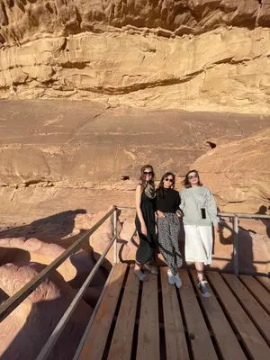 three women standing on a wooden walkway in front of a cliff at Zarb Desert Camp in Wadi Rum