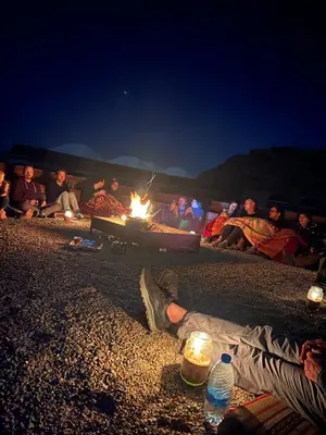 a group of people sitting around a bonfire on the beach at Candle light camp & tours in Wadi Rum