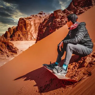 a man sitting on a snowboard in the desert at Candle light camp & tours in Wadi Rum