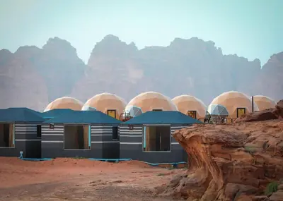 a building in the desert with mountains in the background at Faisal Wadi Rum Camp in Wadi Rum