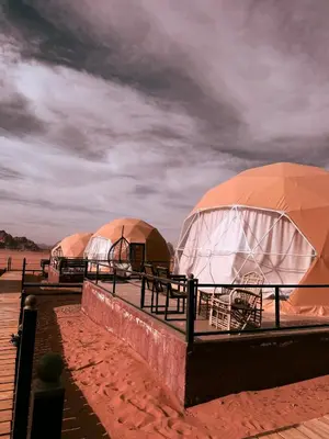 three domed tents on a beach under a cloudy sky at Faisal Wadi Rum Camp in Wadi Rum