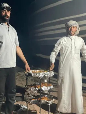 two men standing next to a tray of food at Discover the life of Wadi Rum camp in Wadi Rum