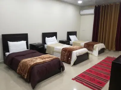 a hotel room with three beds and a red rug at Petra Monastery Tourist Hotel in Wadi Musa