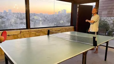 a man standing in a room with a ping pong table at Carob Hostel in Amman