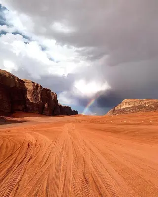 a dirt road in the middle of a desert with a rainbow at Wadi rum desert breath in Wadi Rum