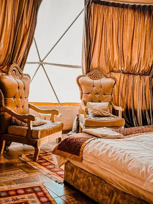 a bedroom with a bed and a chair and curtains at Rum warm bubble camp in Wadi Rum
