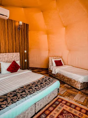 two beds in a room with orange walls at Rum warm bubble camp in Wadi Rum