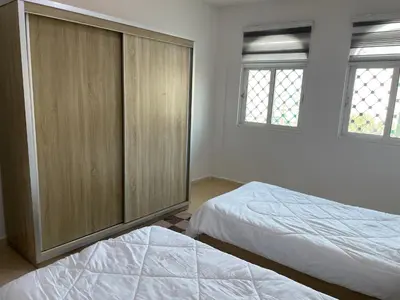 a bedroom with two beds and a cabinet and two windows at Oskar Appartment 2 in Wadi Musa