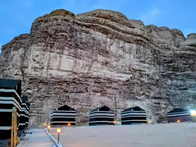 a large rock wall with a building in front of it at Wadi rum galaxy camp in Wadi Rum