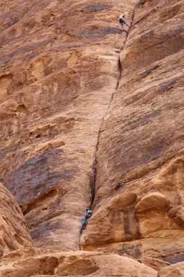 two people are climbing up a rock wall at Arena Desert Camp & Adventurers in Wadi Rum