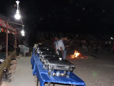 a row of tables in front of a fire at night at Wadi Ghwere Camp مخيم وادي الغوير in Al Khuraybah