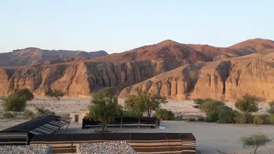 a group of benches in a desert with mountains at Wadi Ghwere Camp مخيم وادي الغوير in Al Khuraybah